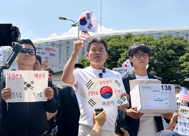 ‘부정선거 음모론 윤어게인 유튜버’ 전한길(가운데) 전 한국사 강사와 그 지지자들이 지난 6월 12일 개표소 봉쇄 시위 현장인 서울 송파구 SK핸드볼경기장 앞에서 잠실7동 제2투표소에 보관돼 있다 사라진 투표용지 보관상자 중 1개를 제보를 통해 확보했다고 주장하며 상자를 공개하고 있다. [연합뉴스]