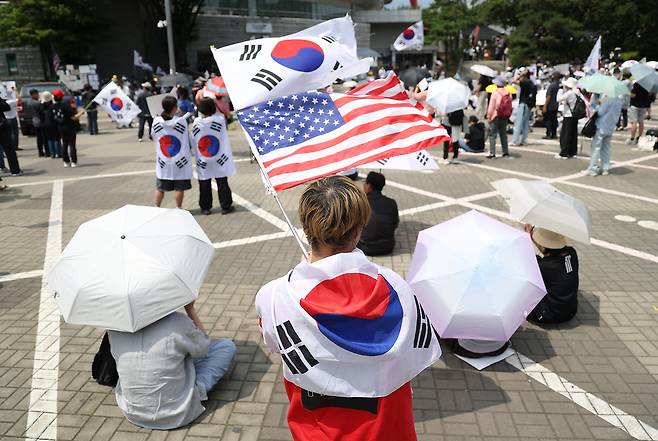 6·3 지방선거 투표용지 부족 사태를 규탄하며 재선거를 요구하는 ‘잠실 개표소 봉쇄 시위’가 계속되고 있는 9일 서울 송파구 올림픽공원 핸드볼경기장에서 한 참가자가 태극기와 성조기를 흔들고 있다. 연합뉴스