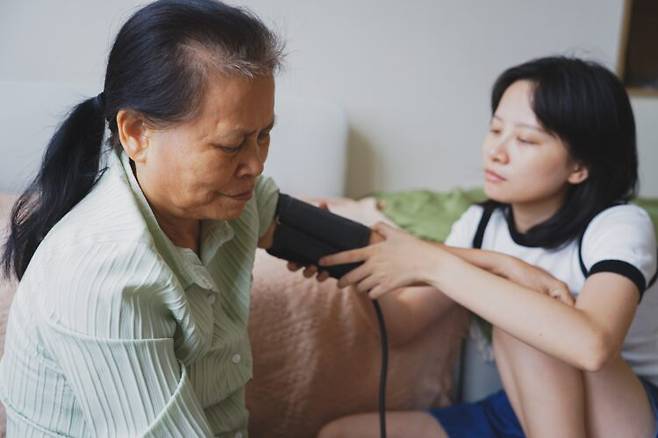한 여성이 집에서 어머니의 혈압을 재고 있다. 노인 혈압은 숫자만 볼 게 아니라 걷는 속도, 손힘, 피로감 같은 몸의 변화와 함께 살펴야 한다. 사진=게티이미지뱅크
