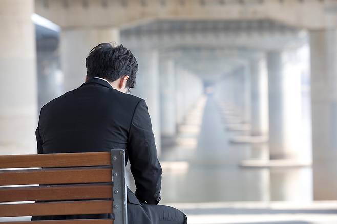 한 남성이 정장을 입은 채 강가 앞 벤치에 앉아 고개를 숙이고 있다. 클립아트코리아