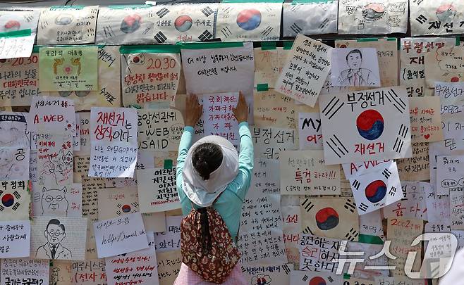 6·3 지방선거 투표용지 부족사태로 인한 '잠실 봉쇄시위'가 25일째를 맞은 25일 서울 송파구 올림픽공원 핸드볼경기장에서 참가자가 매표소 건물에 메시지를 적은 종이를 붙이고 있다. 2026.6.29 ⓒ 뉴스1 구윤성 기자