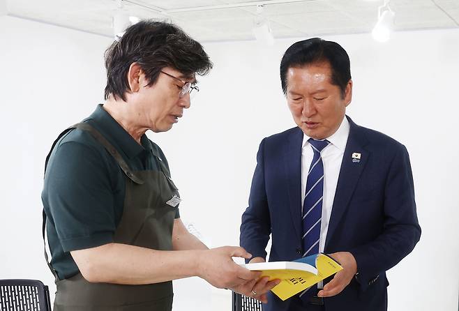 정청래 더불어민주당 대표가 지난 4월 24일 서울 성동구 언더스탠드에비뉴에 마련된 청각 장애인 수제화 브랜드 ‘아지오’ 매장 오픈 행사에 참석, 유시민 작가로부터 책을 전달받고 있다. [연합]