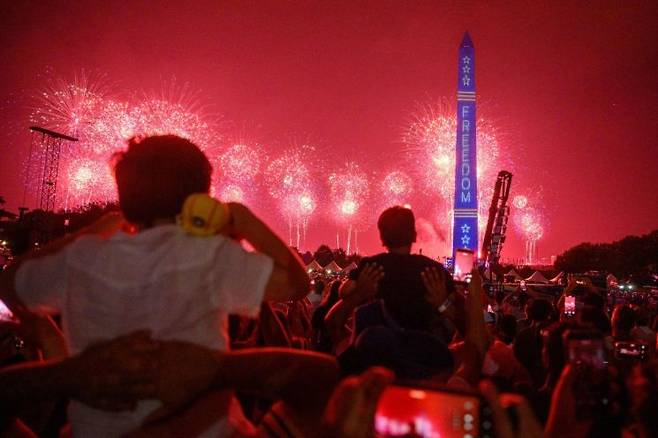 2026년 7월 4일 미국 워싱턴DC 내셔널몰 일대에서 폭우 등 악천후로 중단됐던 행사가 재개된 뒤, 빨간색·흰색·파란색 옷을 입은 시민들이 '그레이트 아메리칸 스테이트 페어' 현장에서 불꽃놀이를 지켜보고 있다. AFP연합뉴스