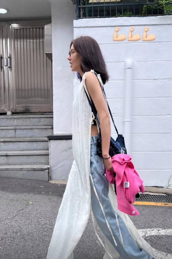 Singer and actress Son Dam-bi has drawn attention by showcasing a stylish layered look featuring a uniquely designed knit top reminiscent of an apron. Son Dam-bi shared an update on her recent visit to a restaurant via her personal social media channel, revealing a fashion style that is both comfortable and full of personality.In the photos, Son Dam-bi paired a white sleeveless knit top with wide-leg denim pants to create a sophisticated look. In particular, the knit fabric, which draped long in the front and back, created a unique silhouette that looked as if she were wearing an apron, capturing everyones attention.She accessorized with a black shoulder bag and horn-rimmed glasses, and added a pink jacket to complete the fresh color palette. Son Dam-bi shared a glimpse of her relaxed daily life, noting that she had spent a pleasant time with a friend.Meanwhile, Son Dam-bi married former speed skater Lee Kyu-hyuk in 2022 and is currently the mother of a daughter. She actively shares her daily life with her family and communicates with fans through her personal social media accounts and YouTube channel.