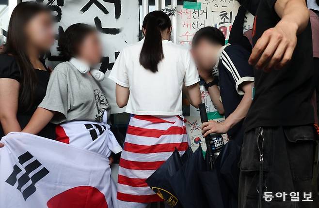 16일 서울 송파구 올림픽공원 핸드볼경기장 앞에서 6·3 지방선거 투표용지 부족 사태를 규탄하는 집회가 열린 가운데, 흰옷을 입고 성조기를 허리에 두른 여성(가운데)이 경기장 문을 잡고 버티고 있다. 이날 경기장에 입주한 대한체육회 산하 체육단체 관계자는 집회 참가자들과 ‘생중계 카메라 대동’ 등의 조건에 합의하고 건물에 진입하려 했지만 이 여성이 비켜주지 않아 끝내 들어가지 못했다. 변영욱 기자 cut@donga.com