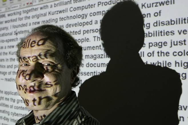 2005년 레이 커즈와일이 자신의 인터넷 사이트 문구가 투사된 스크린 앞에 서 있다. ⒸAP Photo