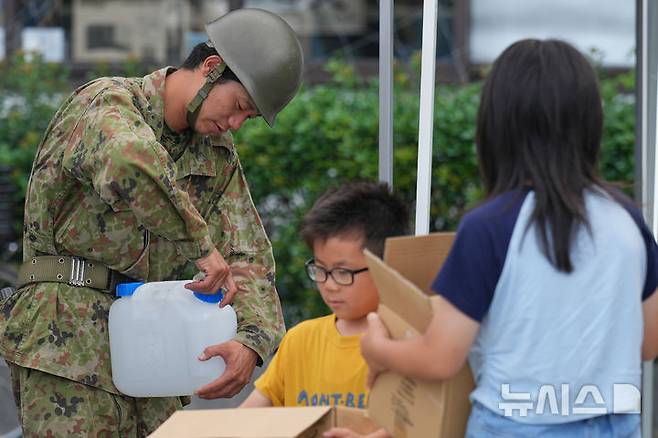 [구마모토=AP/뉴시스]규모 7.1 강진이 강타한 일본 구마모토현 히카와에 위치한 히카와 마을회관에서 자위대원이 현지 주민들에게 급수 지원을 하고 있다. 2027.07.30.