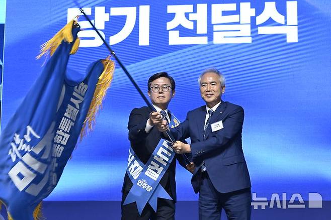[나주=뉴시스] 양시원 기자 = 15일 오후 전남광주 나주시 종합스포츠파크 다목적체육관에서 열린 더불어민주당 전남광주통합특별시당 정기당원대회에서 초대 민주당 전남광주시당위원장으로 선출된 안도걸 당선인(왼쪽)과 양부남 의원이 시당기를 흔들고 있다.  2026.08.15. goodwrite97@newsis.com