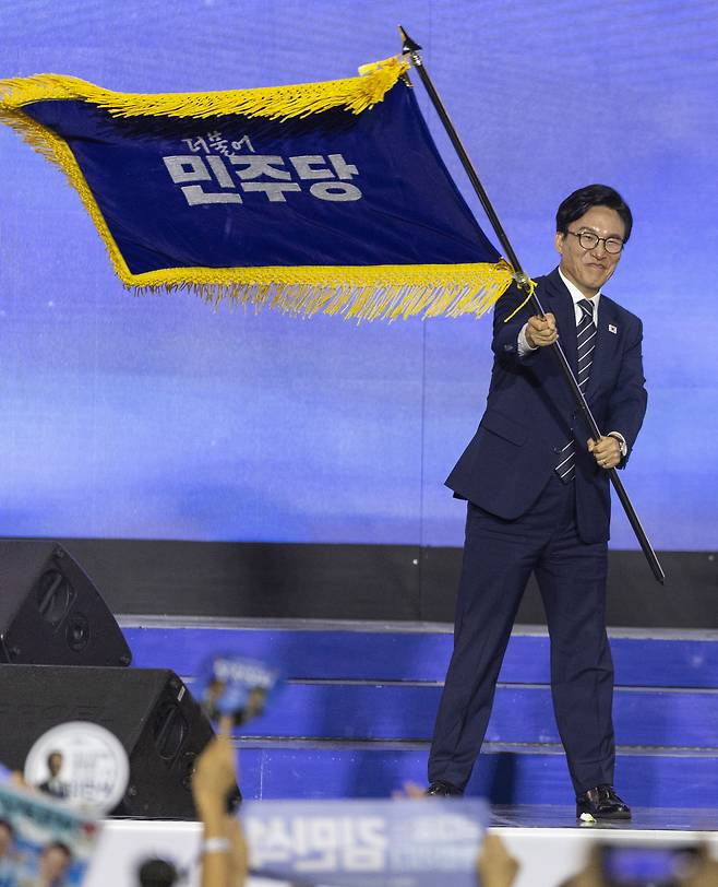 더불어민주당 신임 당 대표에 선출된 김민석 전 총리가 17일 대전 컨벤션센터에서 열린 제3회 더불어민주당 정기 전국당원대회에서 한병도 원내대표에게 전달받은 당 깃발을 흔들고 있다. [연합]