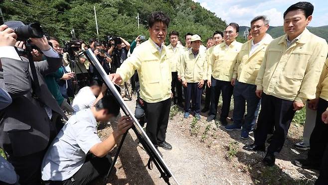 장동혁 국민의힘 대표가 지난 14일 오전 경남 밀양시 웅동저수지를 방문해 한국농어촌공사 관계자로부터 보고받는 동안 실무자로 보이는 직원 2명이 상황판 뒤에 쪼그려 앉아 거치대를 붙잡고 있다. 이날 현장 기온은 34도였다. ⓒ연합뉴스