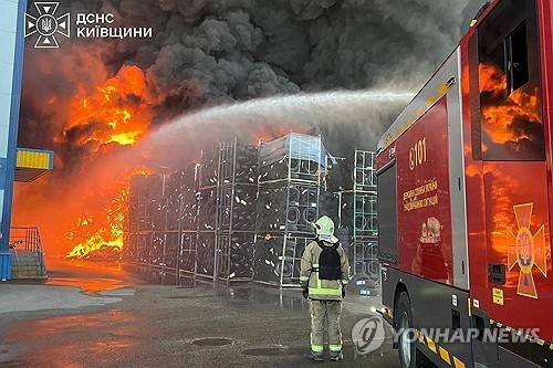 우크라이나 국가비상사태국이 촬영해 제공한 사진. 우크라이나 키이우주(州)의 위치가 알려지지 않은 한 장소에서 공습으로 인해 창고 화재가 발생한 가운데, 한 구조대원이 물을 뿜어내는 소방차 옆에 서서 화재 진압 작업을 벌이고 있다. [AFP 연합뉴스. 재판매 및 DB 금지]