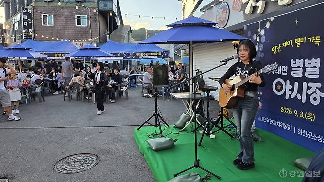 ◇3일 밤 화천군 사내면 사창리에서 처음으로 열린 '별별 야시장'에 지역 주민들 1,000여명이 북적이며 성황을 이뤘다. 사진은 사내면의 한 중학생이 축하무대에 올라 통키타를 치며 가요를 부르고 있는 모습. 화천=이무헌기자