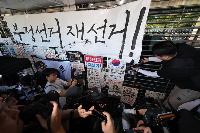 6·3 지방선거 투표용지 부족 사태로 촉발된 잠실 개표소 봉쇄 시위가 이어진 8일 서울 송파구 올림픽공원 핸드볼경기장에서 경찰이 진입을 위해 '부정선거 재선거'라는 문구가 적힌 종이를 제거하고 있다. 연합뉴스