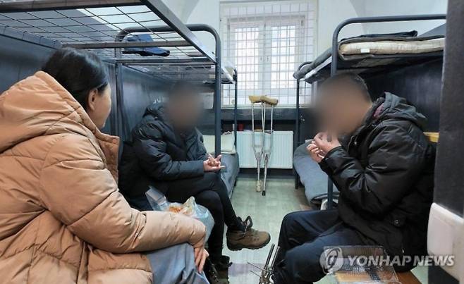 2025년 10월 28일(현지시간) 우크라이나군에 생포된 북한군 포로 백모씨와 리모씨가 우크라이나 내 포로수용소에서 김영미PD와 접견하며 탈북민단체들이 보낸 북한음식 ‘두부밥’을 먹고 있다. 침대(왼쪽 상단)에 이들이 직접 그린 김정은 북한 국무위원장의 초상화가 붙어 있다. 연합뉴스