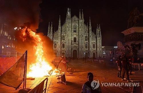 17일(현지시간) 고물가 항의 시위 여파로 불길이 치솟는 밀라노 대성당 앞 광장. AP 연합뉴스