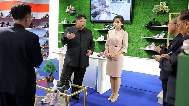 김정은 북한 국무위원장이 지난 19일 '전국피복, 신발전시회-2026'을 찾아 신발 전시대에서 딸 주애가 지켜보는 가운데 간부들과 이야기하고 있다. [조선중앙TV 화면]
