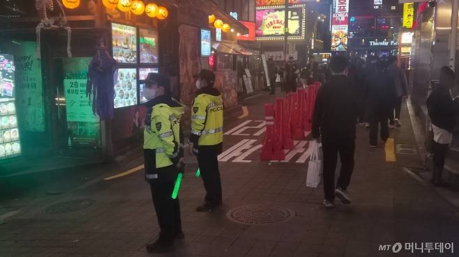 30일 밤 서울 용산구 이태원 세계음식문화거리에서 경찰관들이 시민들에게 통행 방향을 안내하고 있다. 거리 중앙에는 양방향 보행 동선을 구분하기 위한 안전펜스가 설치됐다./사진=김유빈 기자.