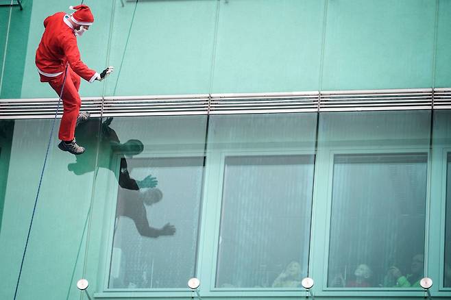 19일(현지시간) 슬로베니아의 수도 류블랴나에 있는 소아과 병원 어린이들에게 산타복장을 한 남성이 빌딩 벽에 매달린 채 손을 흔들며 격려하고 있다.[AFP=연합뉴스]