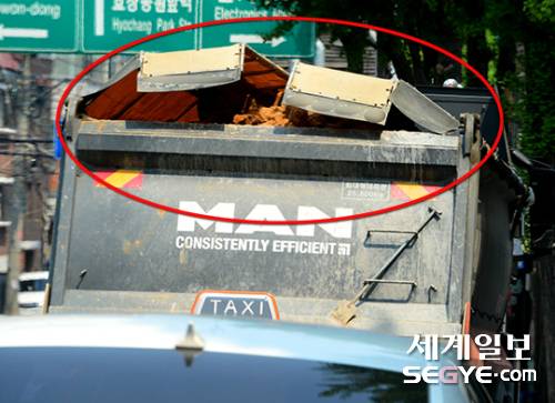 지난달 27일 서울 용산구 한 재래시장 이면도로. 25톤 덤프트럭이 덮개를 제대로 덮지 않은 상태에서 주행하고 있다. 뒤따르는 운전자의 안전을 위협 하고 있어 단속이 절실한 실정이다.