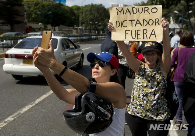 【카라카스(베네수엘라)=AP/뉴시스】초인플레이션에 항의하는 베네수엘라 국민들의 항의 시위가 열리고 있는 카라카스에서 지난 11일 야당 지지 여성 1명이 "독재자 마두로는 사퇴하라"고 쓰인 종이를 든 여성 시위자 앞에서 셀카를 찍고 있다. 니콜라스 마두로 대통령은 14일(현지시간) 또다시 최저임금을 300%나 인상했다. 이는 지난 2년 새 12번째 인상이다. 그러나 마두로에 대한 사퇴 압력은 점점 더 커지고 있다. 2019.1.15