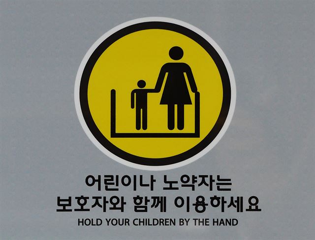 서울 마포구 홍대입구역에 부착된 에스컬레이터 안전 주의 안내표지. 어린이의 보호자로 여성이 그려져 있다.
