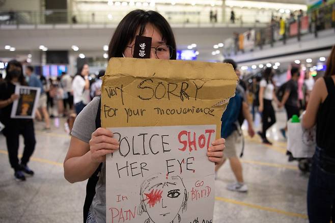 지난 13일 홍콩국제공항에서 한 여성이 안경 위에 안대를 착용한 채 시위를 벌이고 있다. 지난 11일 시위 도중 경찰의 빈백건에 맞아 오른쪽 눈이 실명 위기에 처한 데 대한 항의 차원으로 보인다. 실제 이 여성은 ‘실명 위기 여성’을 상징하는 그림과 함께 “경찰이 그녀의 눈에 총을 쐈다. (공항에서 시위하는 탓에)불편을 끼쳐 죄송하다”며 여행객에게 보내는 글을 함께 적은 팻말을 들고 있다. [EPA]