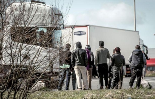프랑스 칼레 항구를 지나는 트럭 사이로 보이는 이민자들. [AFP=연합뉴스]
