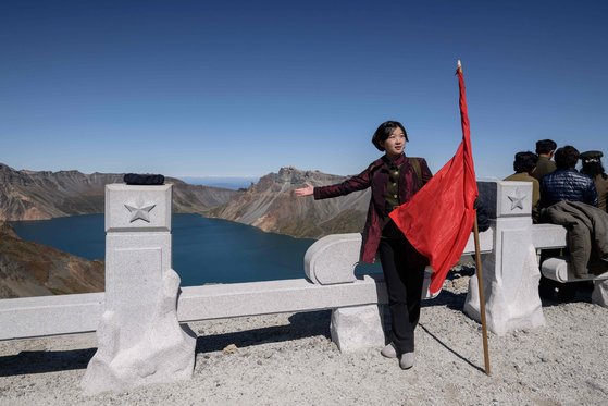 한 북한 학생이 붉은 깃발을 들고 천지를 배경으로 기념촬영하고 있다. [AFP=연합뉴스]