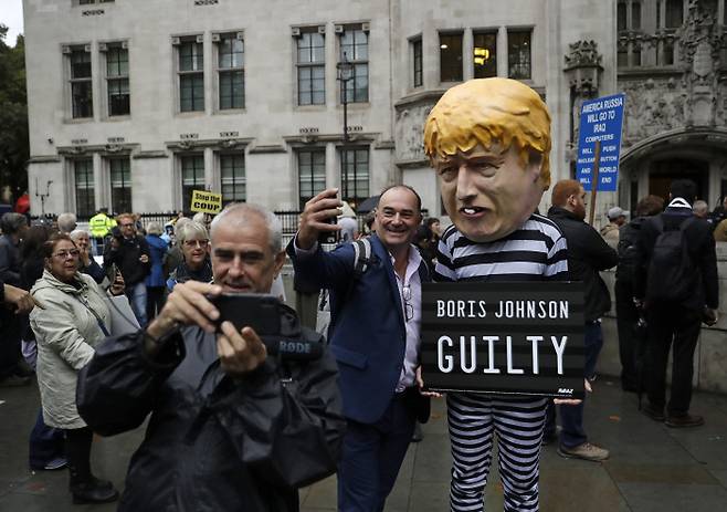 영국 시민들이 24일(현지시간) 런던의 영국 대법원 건물 앞에서 죄수복 차림의 보리스 존슨 영국 총리 인형 앞에서 즐거운 표정으로 사진을 찍고 있다.  런던 | AP연합뉴스