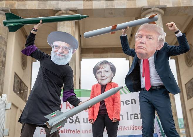 11일(현지시각) 독일 베를린의 브란덴부르크 문 앞에서 열린 반전평화 시위의 참가자들이 이란 최고지도자 아야톨라 하메네이(왼쪽)와 도널드 트럼프 미국 대통령(오른쪽)이 미사일을 들고 대치하는 것을 앙겔라 메르켈 독일 총리(가운데)가 중재하는 상황을 연출한 가면극을 하고 있다. 테헤란/EPA 연합뉴스