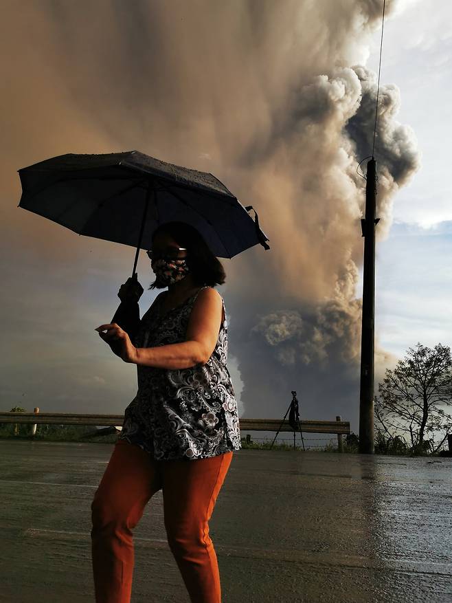 12일(현지시간) 필리핀 따가이따이 인근 지역의 따알 화산이 재를 내 뿜고 있는 가운데 한 주민이 우산을 쓰고 대피하고 있다. [EPA=연합뉴스]