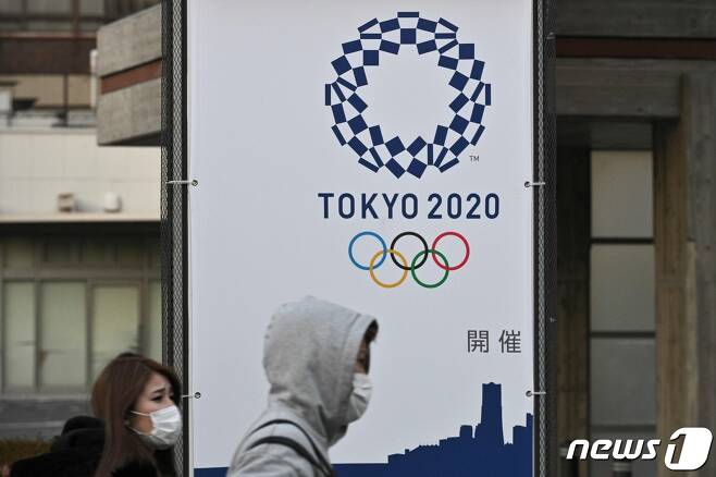 지난 11일 일본 도쿄에서 열린 기자회견에서 마스크를 쓴 기자가 도쿄올림픽 현수막 옆에 서 있다. © AFP=뉴스1