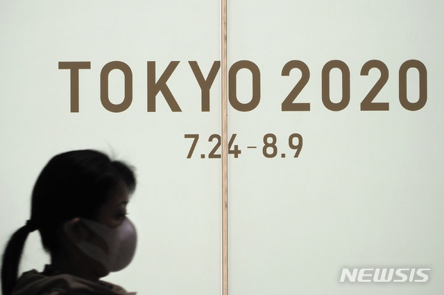 [도쿄=AP/뉴시스]지난 13일(현지시간) 일본 도쿄에서 마스크를 낀 한 여성이 도쿄 2020 올림픽을 홍보하는 화면 앞을 지나고 있다. 2020.03.14.