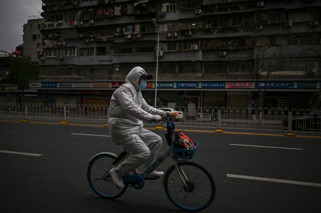 1일 중국 후베이성 우한에서 방호복을 입은 한 남성이 자전거를 타고 텅 빈 도심 차로를 달리고 있다. 우한=AFP 연합뉴스