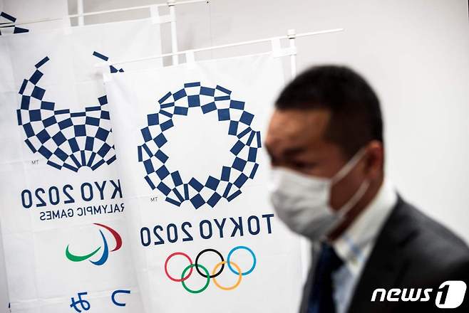 지난달 11일 일본 도쿄에서 열린 기자회견에서 마스크를 쓴 기자가 도쿄올림픽 현수막 옆에 서 있다. © AFP=뉴스1