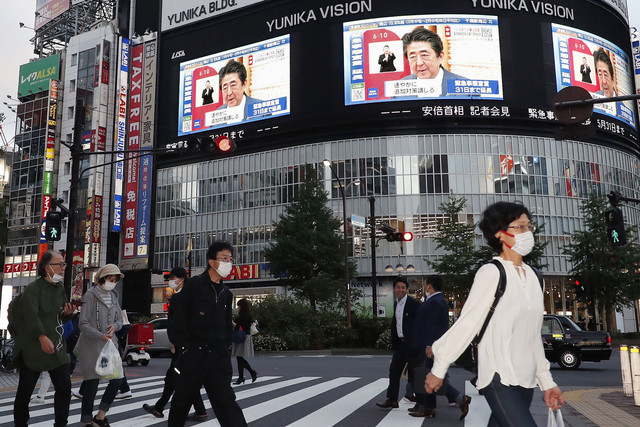 아베 신조 일본 총리가 4일 긴급사태를 31일까지 연장한다고 발표하는 모습이 전광판에 비치는 가운데, 도쿄 거리에서 시민들이 마스크를 쓴 채 걷고 있다. 도쿄/교도 AP 연합뉴스