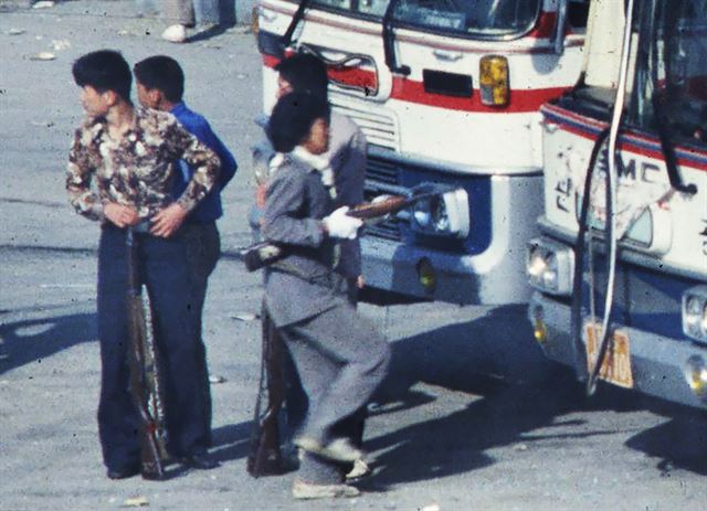 1980년 5월 22일 아침 광주시 외곽 송정리역 광장에서 젊은 남성들 위주의 시위대가 도청으로 출발하기 위해 버스와 트럭에 오르는 가운데 직장 유니폼을 입은 여성이 소총을 들고 버스로 향하고 있다. 박태홍 전 한국일보 기자