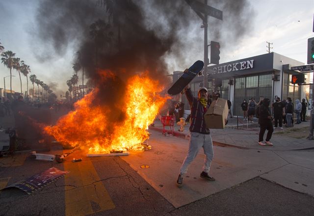 30일 미국 캘리포니아주 로스앤젤레스에서 인종차별 규탄 시위가 벌어진 가운데 한 시위 참가자가 치솟는 화염을 뒤로한 채 분노를 표출하고 있다. 로스앤젤레스=AP연합뉴스