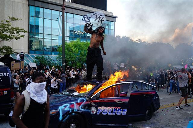 조지 플로이드 사망 사건 규탄 시위가 미 전역으로 확산하는 가운데 30일 조지아주 애틀랜타에서 한 시위 참가자가 불타고 있는 경찰차 위에 올라 경찰 방패를 든 채 분노하고 있다. 애틀랜타=AFP 연합뉴스