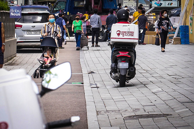 유아차를 끌고가는 한 육아맘 옆으로 배달 오토바이가 지나가고 있다. 도로교통법상 오토바이는 이륜자동차, 즉 '차'의 일종으로 반드시 차도로 주행해야 한다. 김재호 기자 ⓒ베이비뉴스