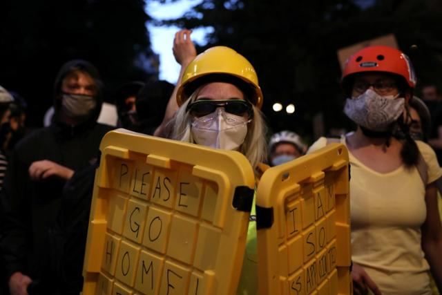 포틀랜드에서 21일 노란 셔츠를 입고 핼멧과 마스크를 쓴 한 여성이 플라스틱 뚜껑을 방패삼아 들고 인종 차별 및 연방요원 파견 반대 시위를 하고 있다. 포틀랜드=로이터 연합뉴스