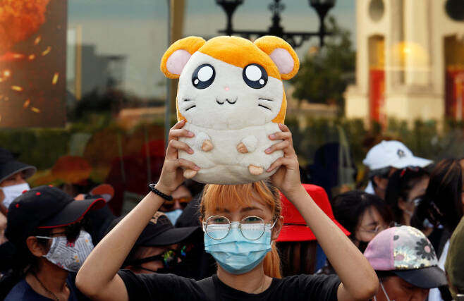 지난달 26일(현지시간) 태국 방콕에서 열린 반정부 시위에 참석한 한 시위자가 일본 만화 ‘햄타로’ 인형을 들고 있다. 시위대는 ‘햄타로’ 주제가를 바꿔 부르며 군사정부의 부패를 비판했다. 방콕｜로이터연합뉴스