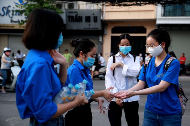 코로나19가 재확산하는 베트남 하노이에서 10일 자원봉사자가 고교 졸업시험을 치르려는 학생들에게 손 소독제를 나눠주고 있다. 하노이=EPA 연합뉴스