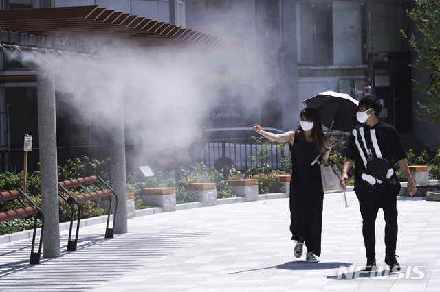 [도쿄=AP/뉴시스]지난 12일 일본 도쿄의 한 거리 수증기 분사 지점에서 코로나19 확산을 막기 위해 마스크를 쓴 남녀가 더위를 식히고 있다. 2020.08.12.