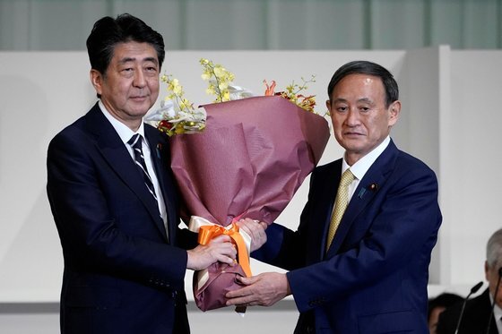 새 총리가 된 스가 요시히데가 아베 신조(왼쪽) 전 일본 총리에게 꽃다발을 선물하고 있다. 두 사람 모두 중국 진출 일본기업의 일본 복귀를 촉구한다. [로이터=연합뉴스]