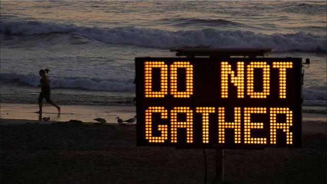 미국 캘리포니아 바닷가에서 한 사람이 공중 보건 표지판을 지나 달리고 있습니다. [사진 출처 :  Mike Blake / Reuters]