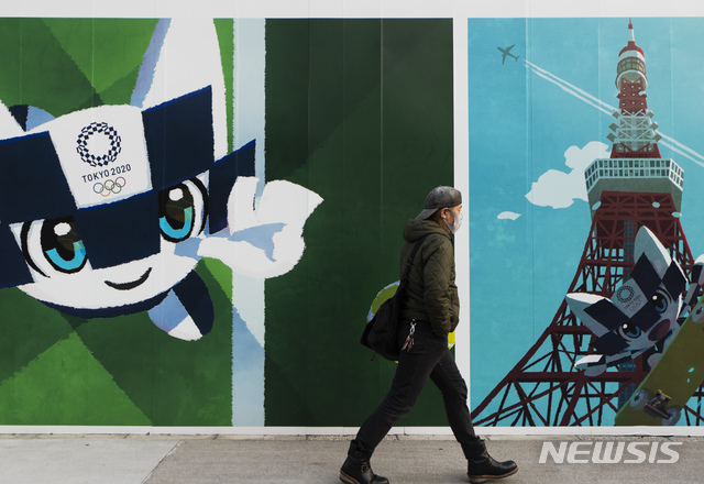 [도쿄=AP/뉴시스]지난 12일 일본 도쿄의 도쿄올림픽 캐릭터가 그려진 벽 앞을 한 시민이 지나가고 있다. 2020.11.13.