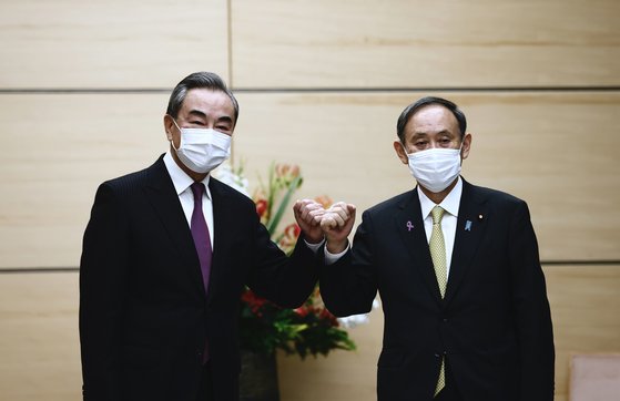 왕이 중국 외교부장이 25일 오후 스가 요시히데 일본 총리와 만나 팔목과 손등을 마주 대며 인사를 나누고 있다. [AP=연합뉴스]