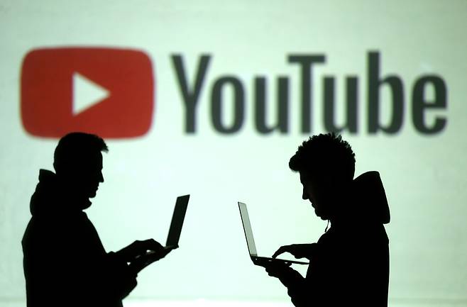 Silhouettes of mobile device users are seen next to a screen projection of YouTube logo (Reuters-Yonhap)