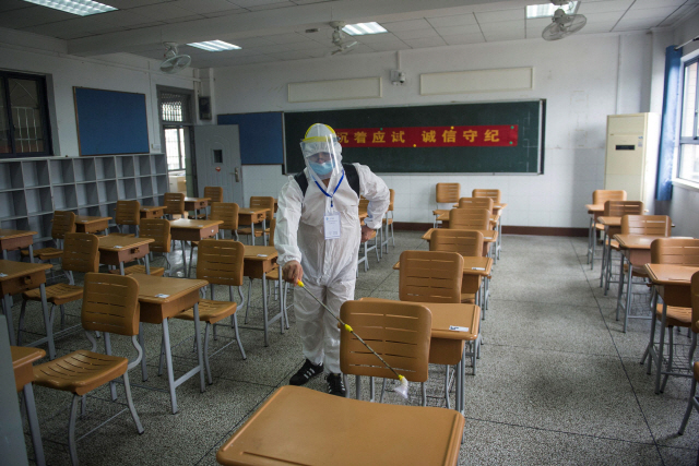 중국 우한의 한 학교에서 보호장구를 착용한 관계자가 교실의 책상과 의자를 소독하고 있다./AFP연합뉴스